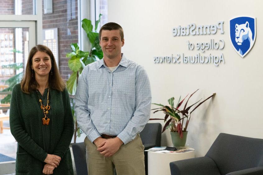 Two people stand in front of a wall that reads "Penn State College of Agricultural Sciences"